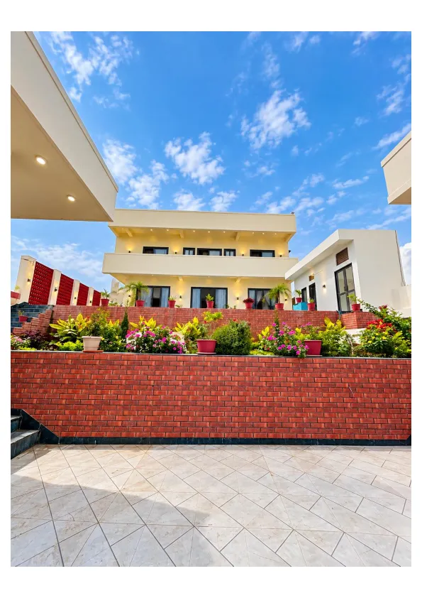Modern 5 bhk villa with a landscaped garden, red brick walls, and a spacious tiled courtyard under blue skies