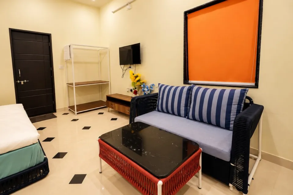 Room with a bed, striped blue sofa, black coffee table, orange blind, wall-mounted TV, and cream tiled floora