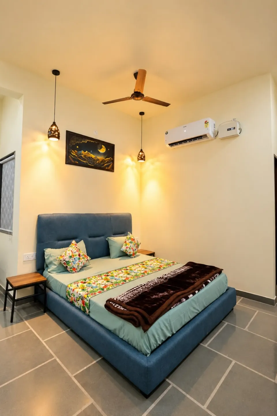 Bright bedroom with a blue platform bed, floral bedding accents, wooden side tables, framed artwork, and a ceiling fan